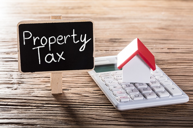 Tiny house model on a calculator with a sign by it that says property tax on a wooden table